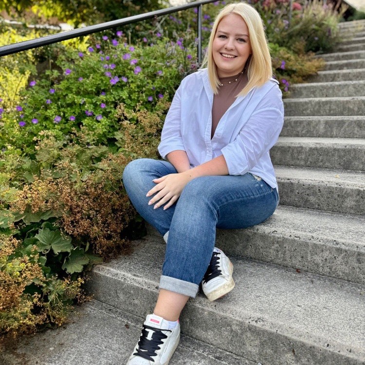 Tamina Piberger von Life in Balance sitzt lächelnd auf einer Steintreppe im Grünen